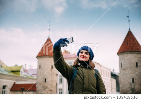 Tallinn, Estonia. Young Caucasian Woman Backpacker Tourist Enjoying Life, Smiling And Using Smartphone Near Landmark Viru Gate. Vacation In Old Town. Girl Surfing Net Internet In Phone Tallinn, Estonia. Young Caucasian Woman Backpacker Tourist Enjoying Life, Smiling And Using Smartphone Near Landmark Viru Gate. Vacation In Old Town. Girl Surfing Net Internet In Phone 135419536
