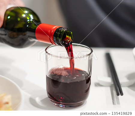 Closeup shot of red wine bottle pouring wine into glass Closeup shot of red wine bottle pouring wine into glass 135419829