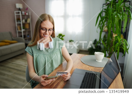 Young woman enjoys online shopping at her cozy home office space 135419949