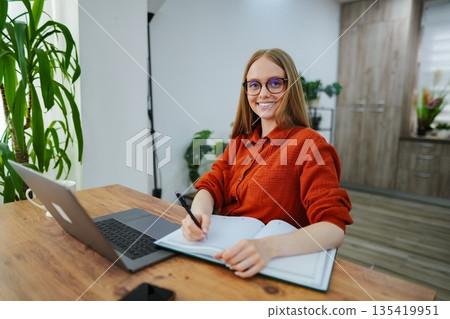 Focused woman writes notes while working at a stylish home office 135419951