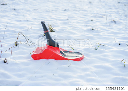 Bright red plastic snow shovel stuck in fresh white snow outdoors, symbolizing winter weather, snowfall, snow removal and cold season chores 135421101