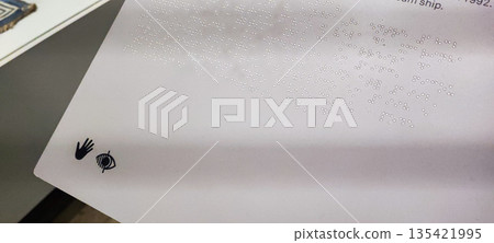 A child's hand explores Braille on a white stand depicting a three-dimensional boat. Concepts of inclusivity, sensory learning, and interactive interaction in educational or museum settings. 135421995