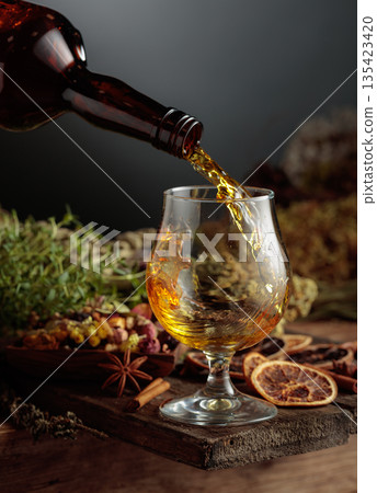 Herbal bitter liqueur is poured from a vintage bottle into a glass. 135423420