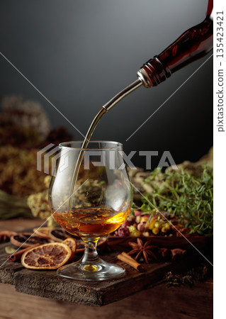 Herbal bitter liqueur is poured from a vintage bottle into a glass. Herbal bitter liqueur is poured from a vintage bottle into a glass. 135423421