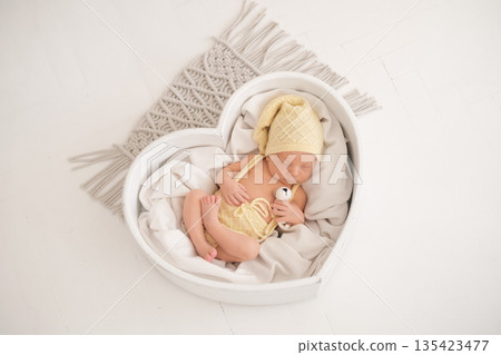 A newborn baby in a heart-shaped basket is sleeping sweetly hugging a toy A newborn baby in a heart-shaped basket is sleeping sweetly hugging a toy 135423477