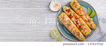 Elotes mexican street corn cob covered in spices and cheese being served on plate Elotes mexican street corn cob covered in spices and cheese being served on plate 135423582