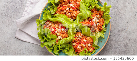 Lettuce wraps filled with minced meat and topped with peanuts and chili pepper flakes on a plate, healthy protein dish 135423600