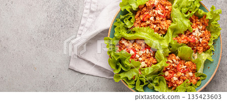 Lettuce wraps filled with minced meat and topped with peanuts and chili pepper flakes on a plate, healthy protein dish, copy space 135423603
