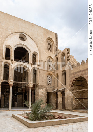 Qalawun complex interior at Al-Muizz Street. Features Islamic architecture with arches, intricate designs, and a central courtyard with greenery. Qalawun complex interior at Al-Muizz Street. Features Islamic architecture with arches, intricate designs, and a central courtyard with greenery. 135424088