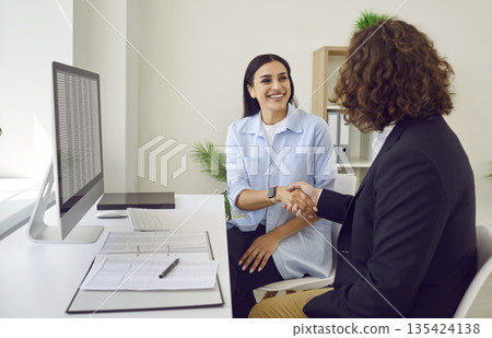 Business people sitting in office on workplace making a deal. Man shaking hand with woman. Business people sitting in office on workplace making a deal. Man shaking hand with woman. 135424138