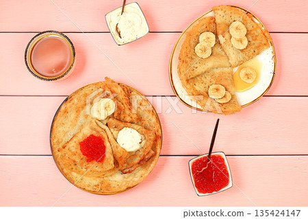 Delicious Russian pancakes with soft cheese, bananas, and red caviar on the kitchen table. Healthy breakfast with fresh ingredients, Maslenitsa concept and traditional Russian cuisine, selective focus 135424147