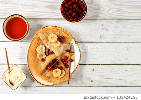 Delicious Russian pancakes with jam, soft cottage cheese, bananas, cranberries, and honey on a marble table. Healthy breakfast made from natural ingredients, Maslenitsa concept, natural products Delicious Russian pancakes with jam, soft cottage cheese, bananas, cranberries, and honey on a marble table. Healthy breakfast made from natural ingredients, Maslenitsa concept, natural products 135424155