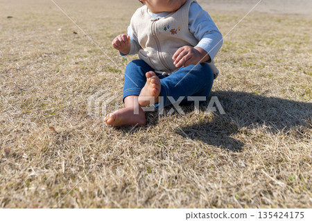 Barefoot baby sitting on the grass 135424175
