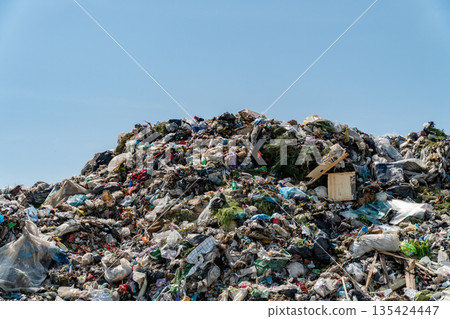 A landfill site shows a large pile of trash and rubbish under a clear blue sky. This location highlights pollution and waste management challenges 135424447