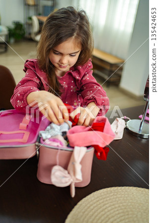 Little girl joyfully exploring a treasure chest of colorful dress-up clothes at home during a sunny afternoon 135424653
