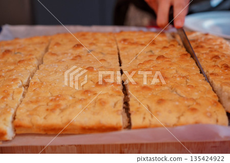 Italian woman cutting homemade Italian focaccia with a knife Italian woman cutting homemade Italian focaccia with a knife 135424922