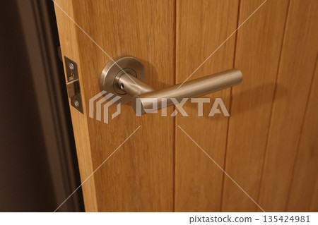 A door handle is shown in a wooden door A door handle is shown in a wooden door 135424981
