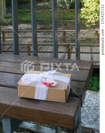 Gift with necklace and lollypop on park bench 135425152