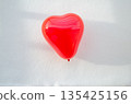 A glossy vibrant red heart shaped balloon floating above fresh snow  a romantic symbol of Valentine's Day in winter. 135425156