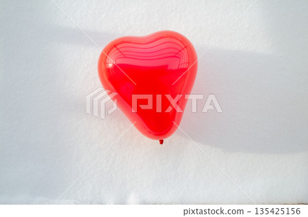 A glossy vibrant red heart shaped balloon floating above fresh snow a romantic symbol of Valentine's Day in winter. A glossy vibrant red heart shaped balloon floating above fresh snow a romantic symbol of Valentine's Day in winter. 135425156