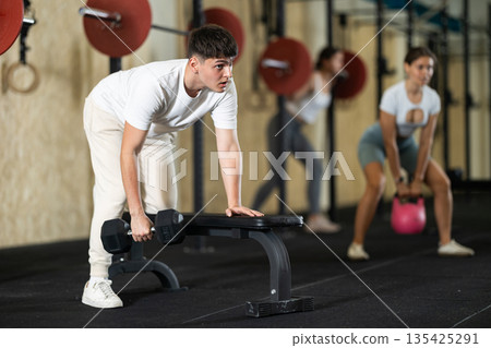 Young guy training with dumbbells on bench 135425291