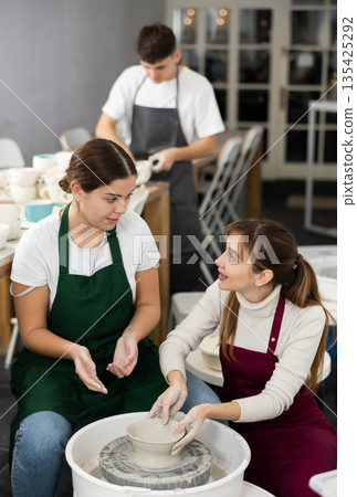 Woman working with pottery wheel and master giving instructions 135425292