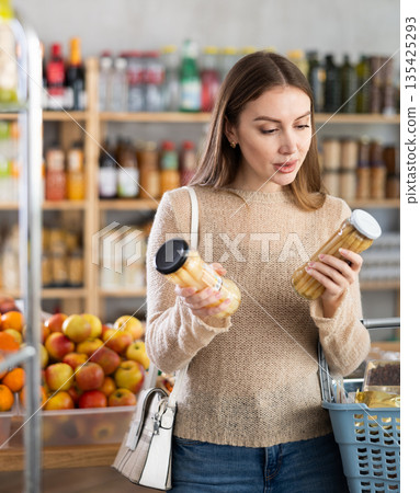 Positive girl with basket in shop holding and choosing asparagus 135425293