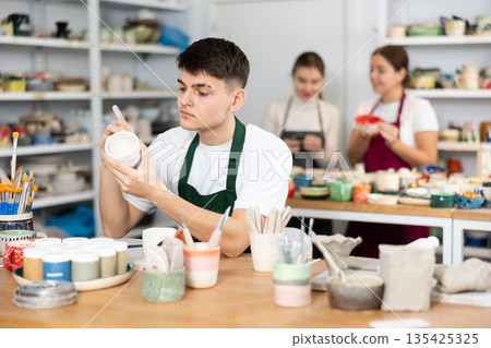 Young man painting pottery in workshop 135425325