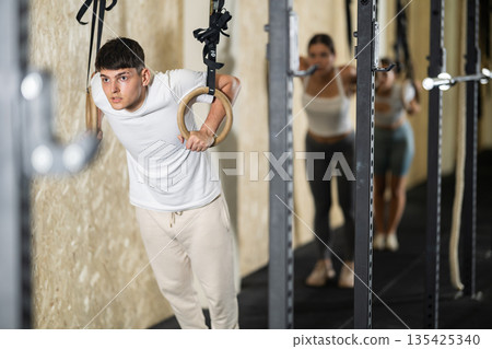 Guy trains on gymnastic rings in modern crossfit gym Guy trains on gymnastic rings in modern crossfit gym 135425340