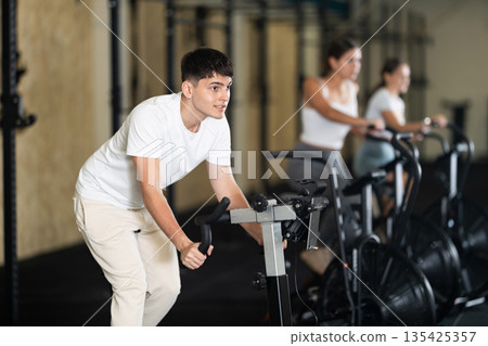 Young guy doing sports on a stationary bike in gym 135425357