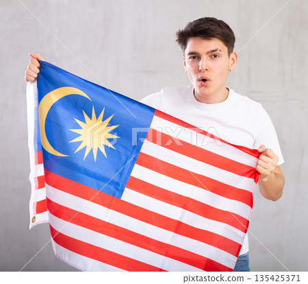 Male fan holds canvas of national Malaysian flag in hands raised above head and chants slogan 135425371
