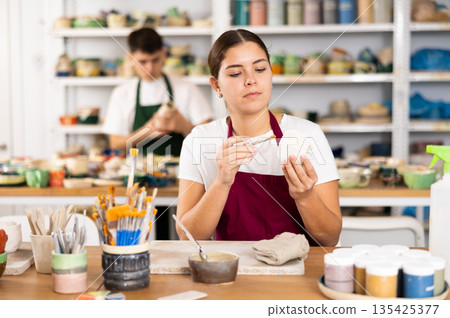 Young woman painting pottery in workshop 135425377