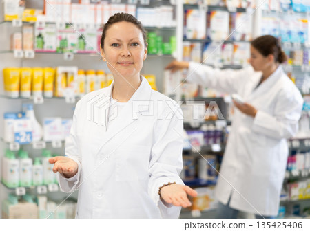 At pharmacy, apothecary waiting for customers and invites with gesture go to department of cosmetics At pharmacy, apothecary waiting for customers and invites with gesture go to department of cosmetics 135425406