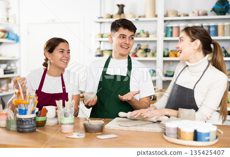 Two young women and young man making pottery 135425407