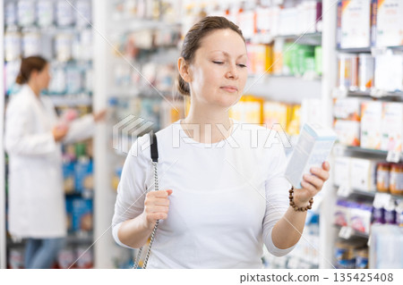 Young female shopper carefully chooses cosmetics in pharmacy 135425408