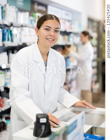 Portrait of female pharmacist at cash register in interior of pharmacy Portrait of female pharmacist at cash register in interior of pharmacy 135425430