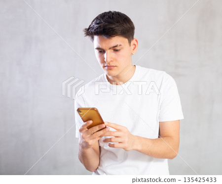 Attentive young man looking at the screen of mobile phone Attentive young man looking at the screen of mobile phone 135425433