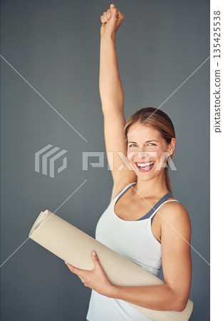 Happy woman, portrait and yoga mat with fist in celebration for healthy exercise against a grey studio background. Excited female person or yogi with smile for winning, fitness or workout success 135425538