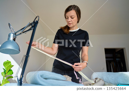 Woman standing indoors measuring fabric with tape measure 135425664