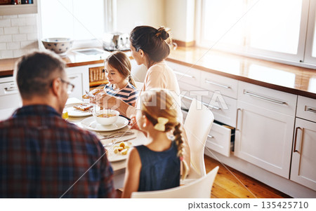 Family, morning and breakfast by table in kitchen for meal, eating or bonding time together at home. Mother, father and children with healthy food to start the day for nutrition or cereal in house 135425710