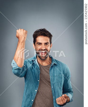 Happy man, fist and celebration for winning, success or victory against a grey studio background. Excited portrait of male person or winner in achievement, win or accomplishment on mockup space 135425902