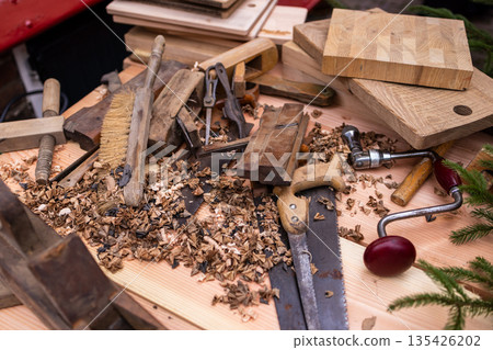 Cluttered woodworking bench with hand saw, brace drill, chisels, and wood shavings, showcasing traditional craftsmanship and active carpentry. 135426202