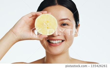 Lemon, face and woman in studio, natural wellness and white background. Happy asian model, beauty portrait and citrus fruits for facial cosmetics glow, vitamin c skincare or detox dermatology results Lemon, face and woman in studio, natural wellness and white background. Happy asian model, beauty portrait and citrus fruits for facial cosmetics glow, vitamin c skincare or detox dermatology results 135426261