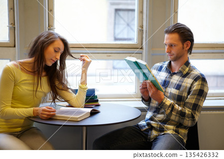 Reading, education and a couple at college in a library for learning, studying and research knowledge. Focus, books and a man and woman at a campus table for a scholarship or school information Reading, education and a couple at college in a library for learning, studying and research knowledge. Focus, books and a man and woman at a campus table for a scholarship or school information 135426332