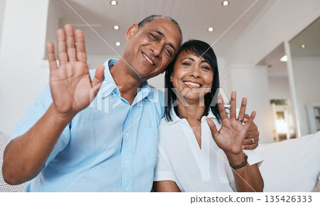 Video call, wave and a senior couple on a sofa in the living room of their home together for communication during retirement. Portrait, smile and a happy mature man with his wife on a virtual chat Video call, wave and a senior couple on a sofa in the living room of their home together for communication during retirement. Portrait, smile and a happy mature man with his wife on a virtual chat 135426333