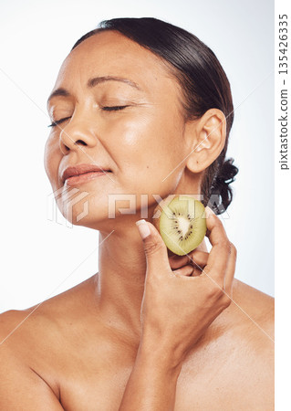 Relax, beauty or mature woman with kiwi for healthy detox, skincare or facial treatment routine in studio. Spa, face or senior model with wellness, self love or fruit isolated on white background Relax, beauty or mature woman with kiwi for healthy detox, skincare or facial treatment routine in studio. Spa, face or senior model with wellness, self love or fruit isolated on white background 135426335