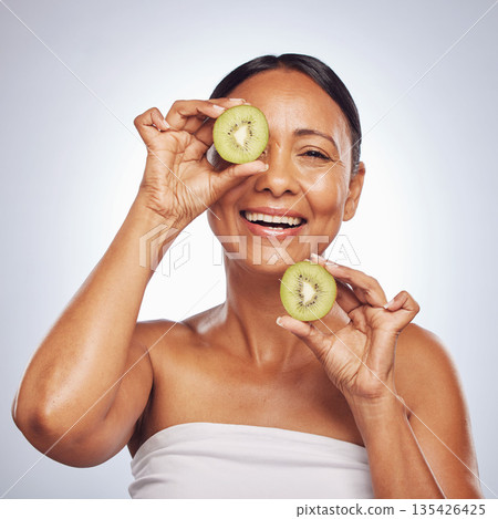 Skincare, face and mature woman with kiwi in studio isolated on a white background. Food, natural fruit and portrait of happy model with nutrition for wellness, healthy diet and beauty for anti aging Skincare, face and mature woman with kiwi in studio isolated on a white background. Food, natural fruit and portrait of happy model with nutrition for wellness, healthy diet and beauty for anti aging 135426425