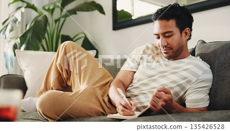 Man, journal and writing on sofa in home, daily reflection or idea notes to relax for creativity. Person, notebook for planning or sketching with agenda in diary, to do list or goal setting at house Man, journal and writing on sofa in home, daily reflection or idea notes to relax for creativity. Person, notebook for planning or sketching with agenda in diary, to do list or goal setting at house 135426528