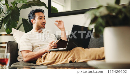 Man, laptop and video call on sofa for remote work from home, earphones and discussion in living room. Person, virtual assistant and computer for online meeting, notebook and feedback at apartment 135426602