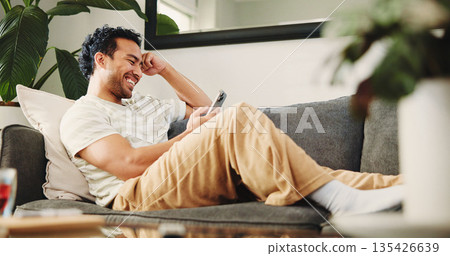 House, smartphone and man on couch, funny and typing with social media, smile and online reading. Laughing, mobile user and Asian person on sofa, cellphone and website info with connection or humor 135426639
